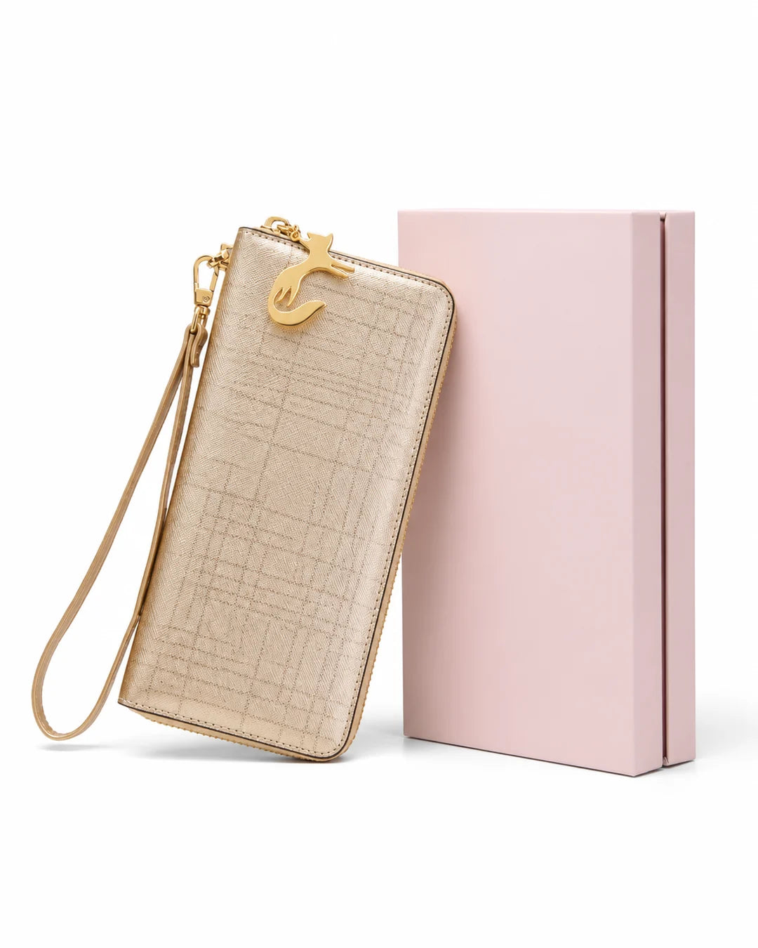 Carteira feminina de couro champagne Aurielle apoiada ao lado de uma caixa rosa, com acabamento texturizado, alça de mão e pingente metálico dourado em formato de gato.