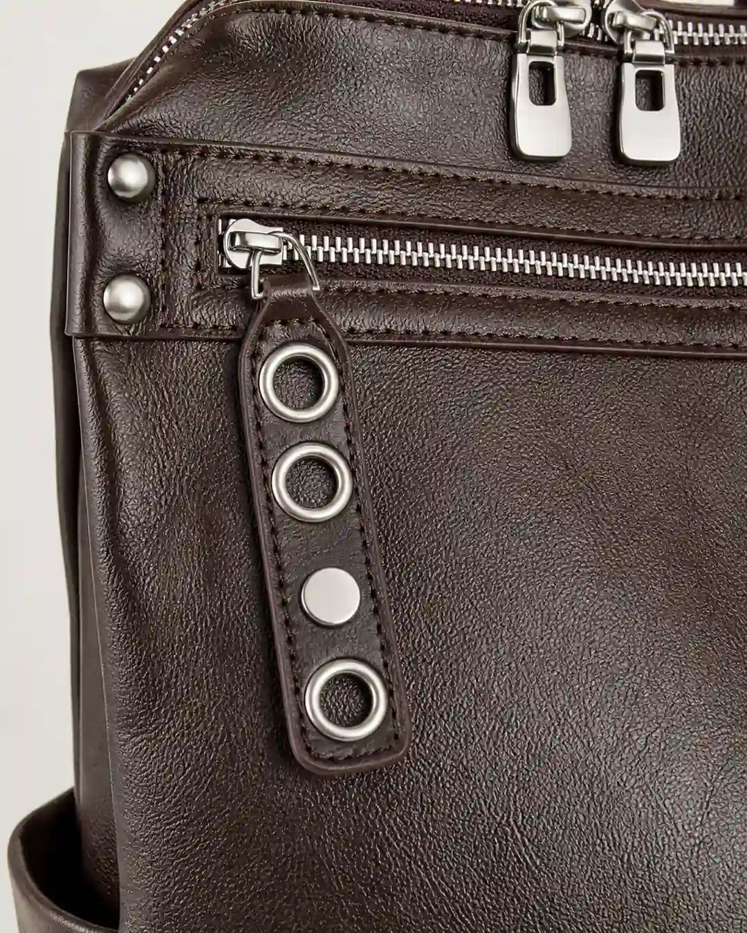 Detalhe da mochila feminina de couro marrom Lorien, destacando o bolso frontal com zíper, os metais decorativos e o acabamento sofisticado.