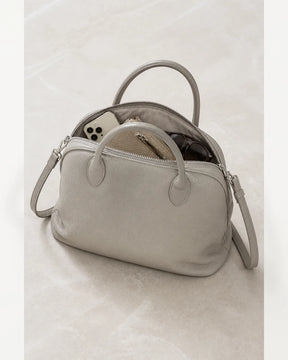 Bolsa feminina de couro cinza claro Vivienne aberta, com celular, carteira e óculos no interior.