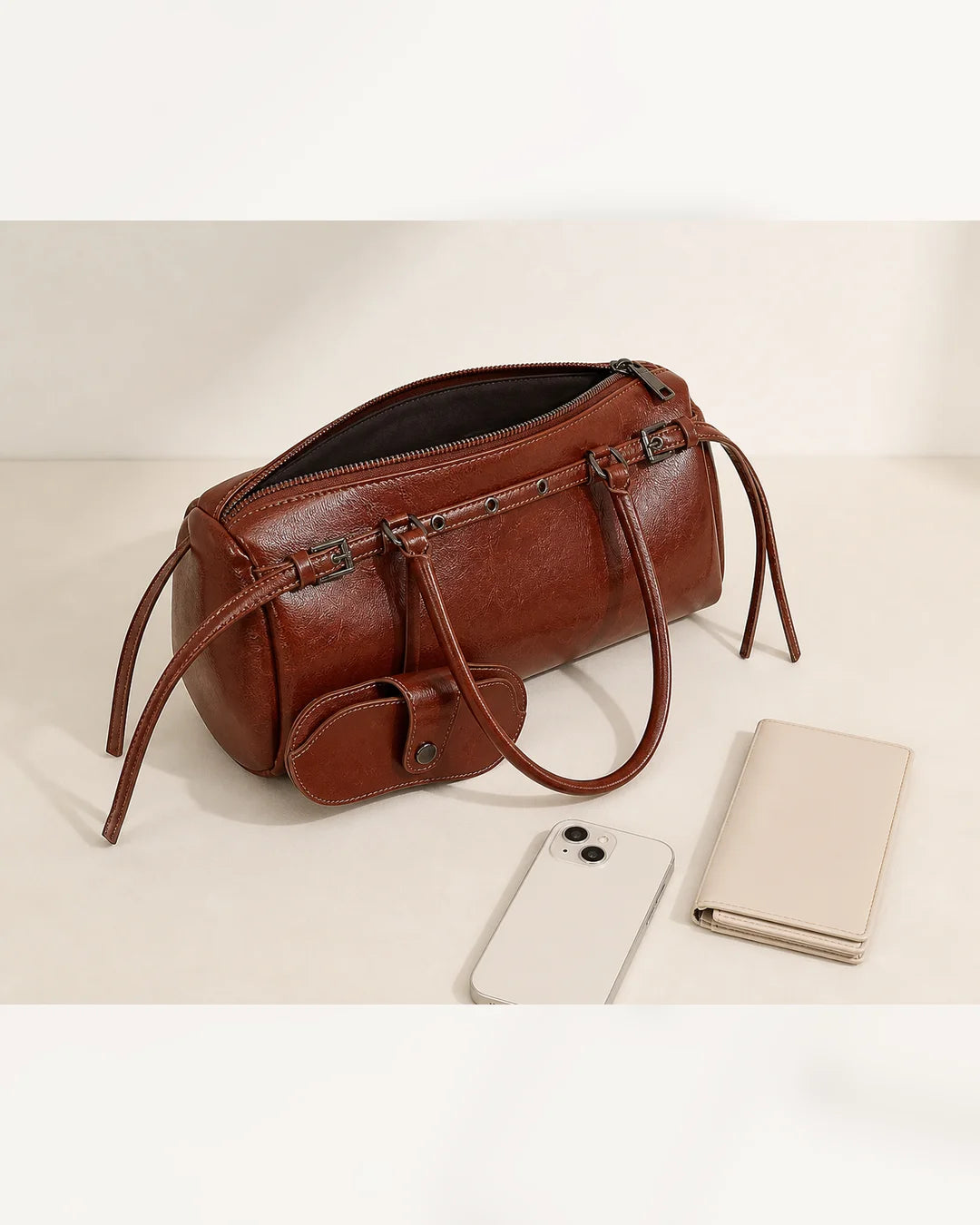 Bolsa feminina de couro marrom Celinne em perspectiva superior, com zíper aberto e itens ao lado, destacando o espaço interno, as alças longas e o porta-óculos acoplado.
