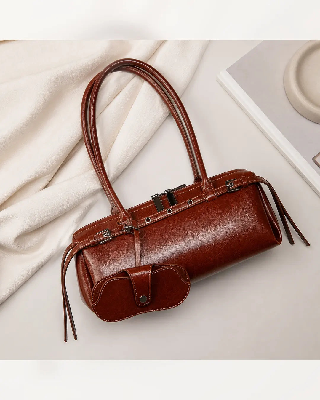 Bolsa feminina de couro marrom Celinne em composição sobre fundo claro, com alças longas, acabamento elegante e porta-óculos acoplado na parte frontal.
