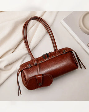 Bolsa feminina de couro marrom Celinne em composição sobre fundo claro, com alças longas, acabamento elegante e porta-óculos acoplado na parte frontal.

