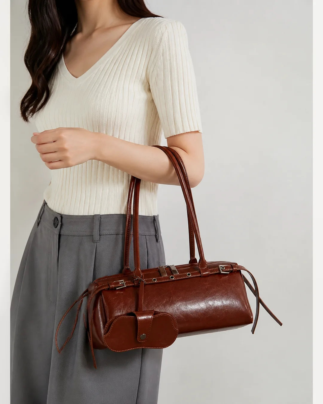 Mulher usando a bolsa feminina de couro marrom Celinne no braço, destacando o tamanho da peça, o caimento das alças e o design sofisticado do modelo.
