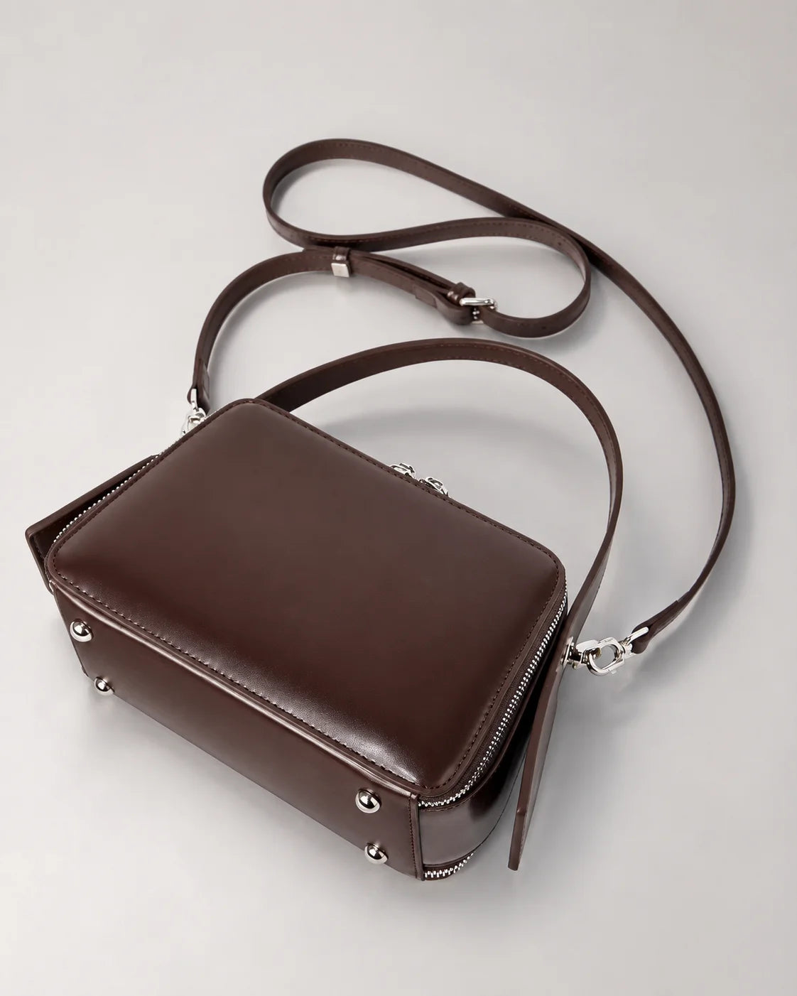 Parte inferior da bolsa feminina de couro marrom Elyra, com pés metálicos na base, alça de mão fixa e alça transversal removível.