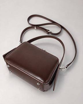 Parte inferior da bolsa feminina de couro marrom Elyra, com pés metálicos na base, alça de mão fixa e alça transversal removível.