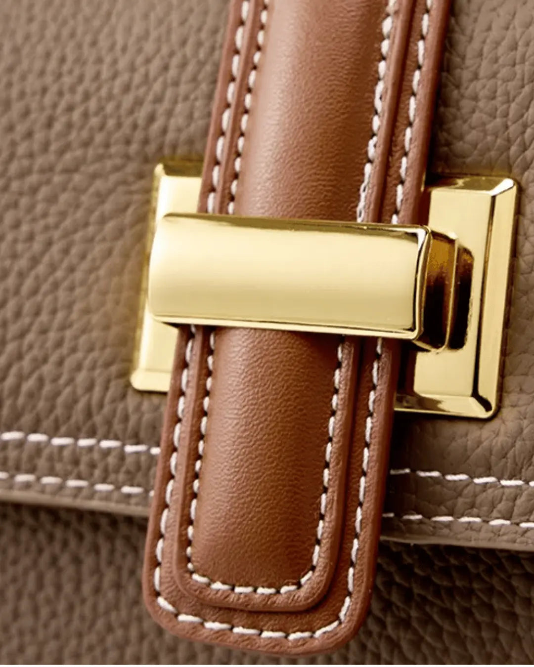 Detalhe do fecho metálico dourado da bolsa feminina Maelle em couro marrom, com acabamento caramelo e costuras claras aparentes.