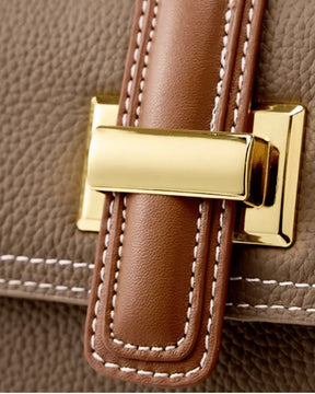 Detalhe do fecho metálico dourado da bolsa feminina Maelle em couro marrom, com acabamento caramelo e costuras claras aparentes.