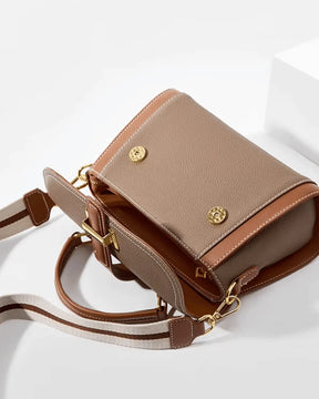 Bolsa feminina Maelle em couro marrom aberta, mostrando o espaço interno, o fechamento magnético, a alça de mão e a alça transversal larga listrada.