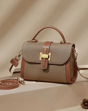 Bolsa feminina Maelle em couro marrom, vista angular em cenário bege, com fecho dourado, alça de mão e alças transversais removíveis fina e larga listrada.