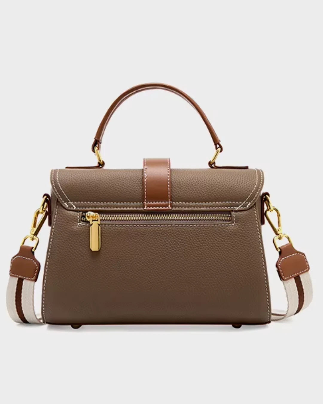 Bolsa feminina Maelle em couro marrom, vista traseira, com alça de mão, alça transversal larga listrada, ferragens douradas e bolso externo com zíper.