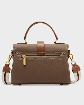 Bolsa feminina Maelle em couro marrom, vista traseira, com alça de mão, alça transversal larga listrada, ferragens douradas e bolso externo com zíper.