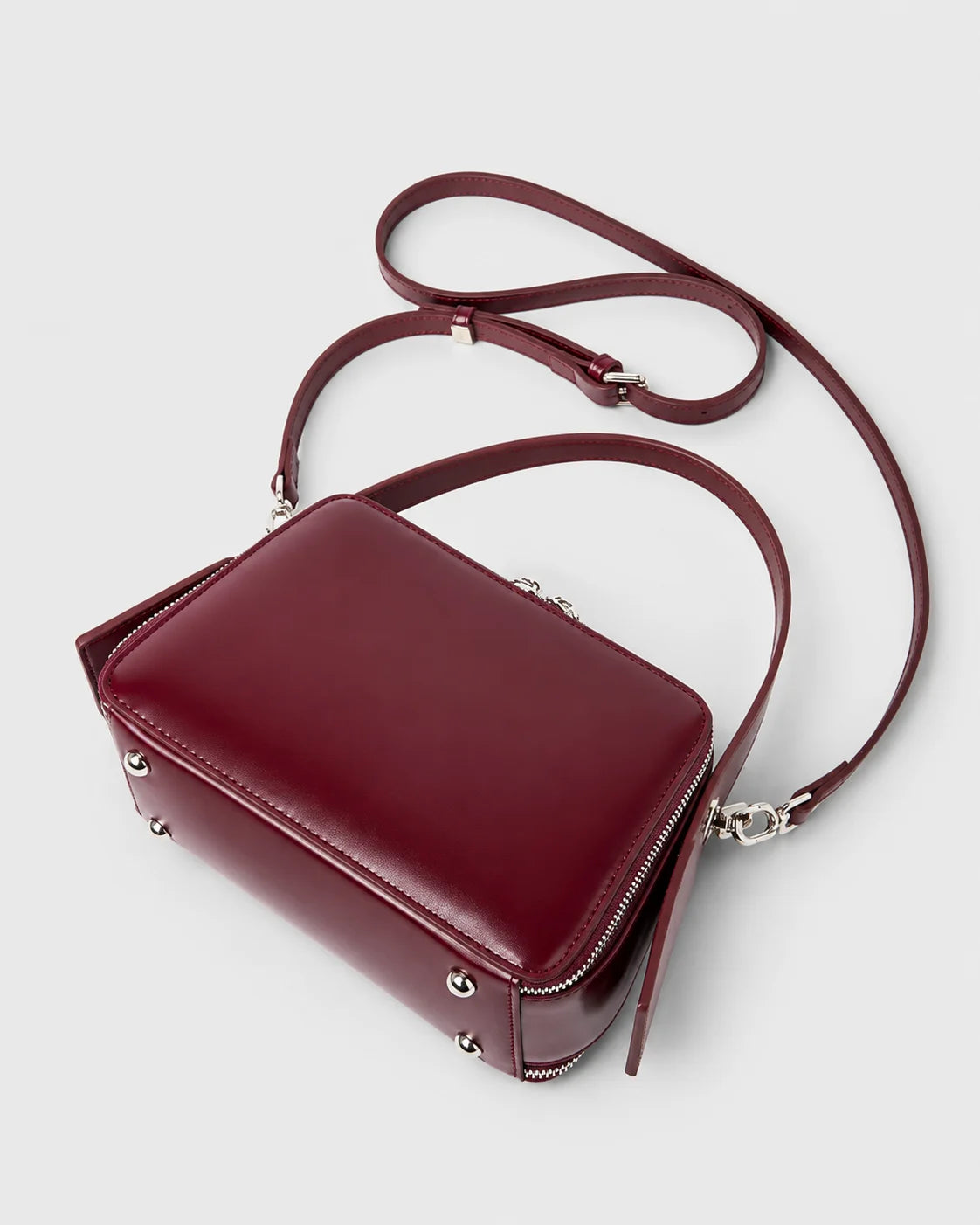 Parte inferior da bolsa feminina de couro marsala Elyra, com pés metálicos na base, alça de mão fixa e alça transversal removível.