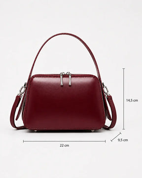 Bolsa feminina de couro marsala Elyra, vista frontal, com alça de mão, alça transversal removível e indicação das medidas de 22 cm de largura, 14,5 cm de altura e 9,5 cm de profundidade. 