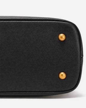 Detalhe da base da bolsa feminina Aveline em couro preto, mostrando o acabamento estruturado, o contorno reforçado e os pés metálicos dourados.