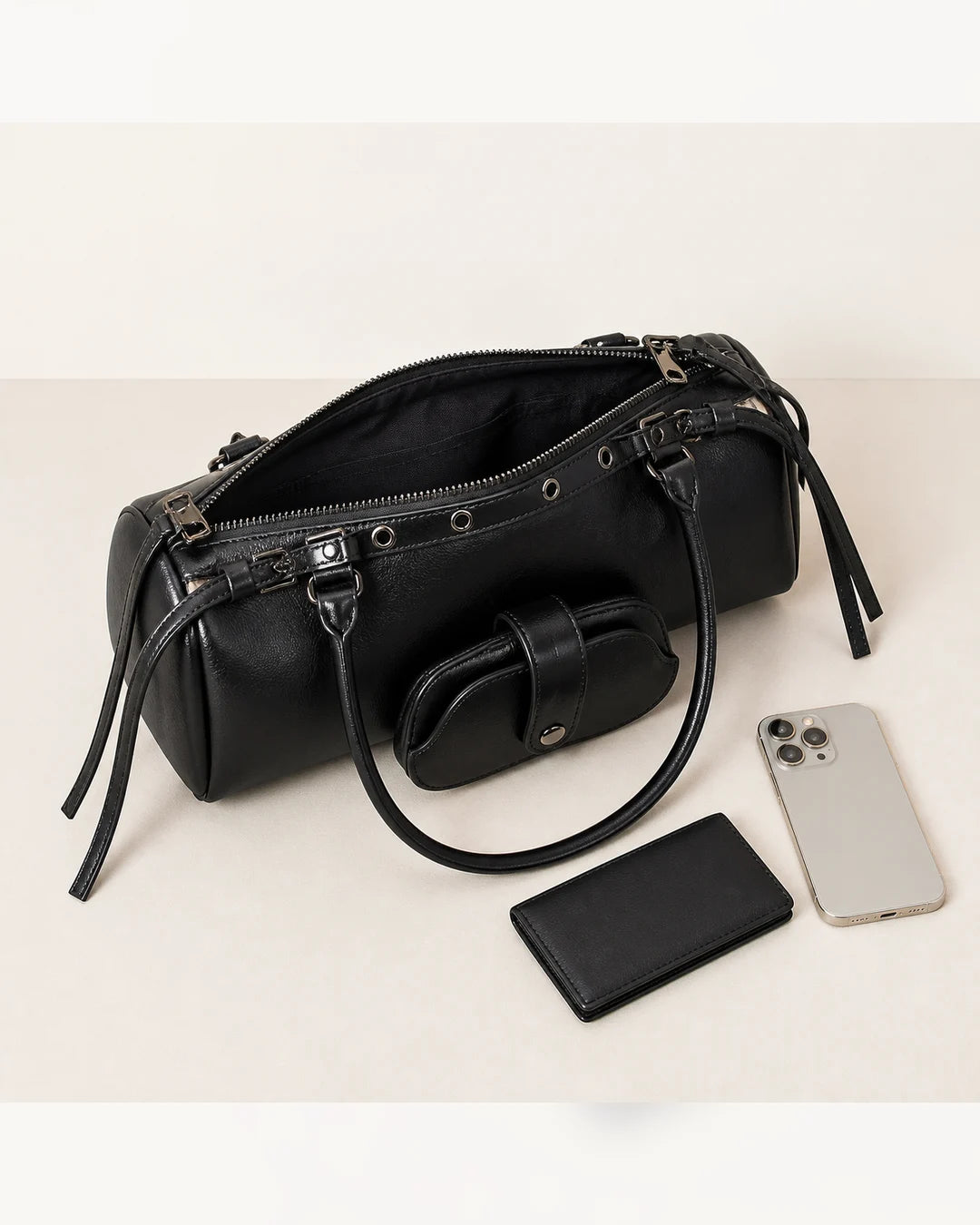 Bolsa feminina de couro preta Celinne em perspectiva superior, com zíper aberto e itens ao lado, destacando o espaço interno, as alças longas e o porta-óculos acoplado.
