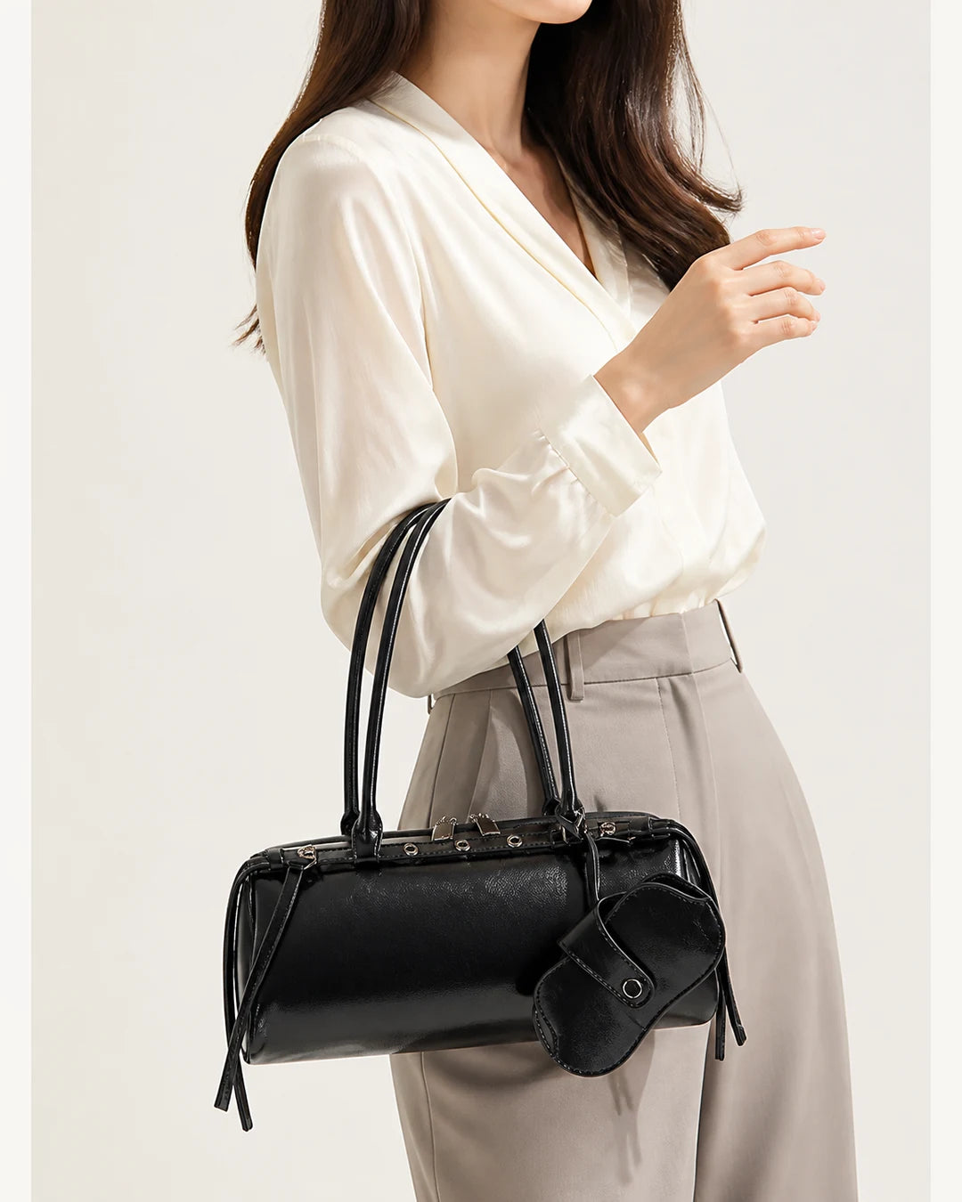 Mulher usando a bolsa feminina de couro preta Celinne no braço, destacando o tamanho da peça, o caimento das alças e o visual elegante do modelo.
