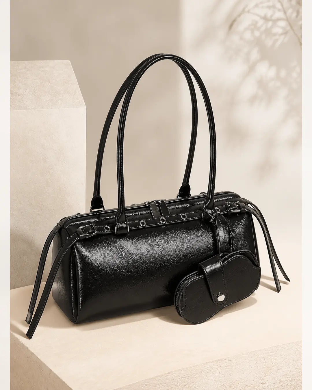 Bolsa feminina de couro preta Celinne posicionada sobre uma base clara, com alças estruturadas, detalhes metálicos e porta-óculos combinando preso à frente.
