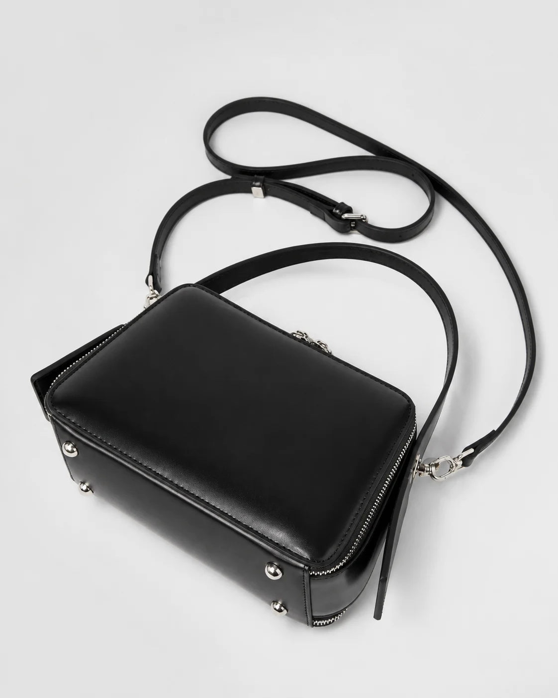 Parte inferior da bolsa feminina de couro marrom Elyra, com pés metálicos na base, alça de mão fixa e alça transversal removível.