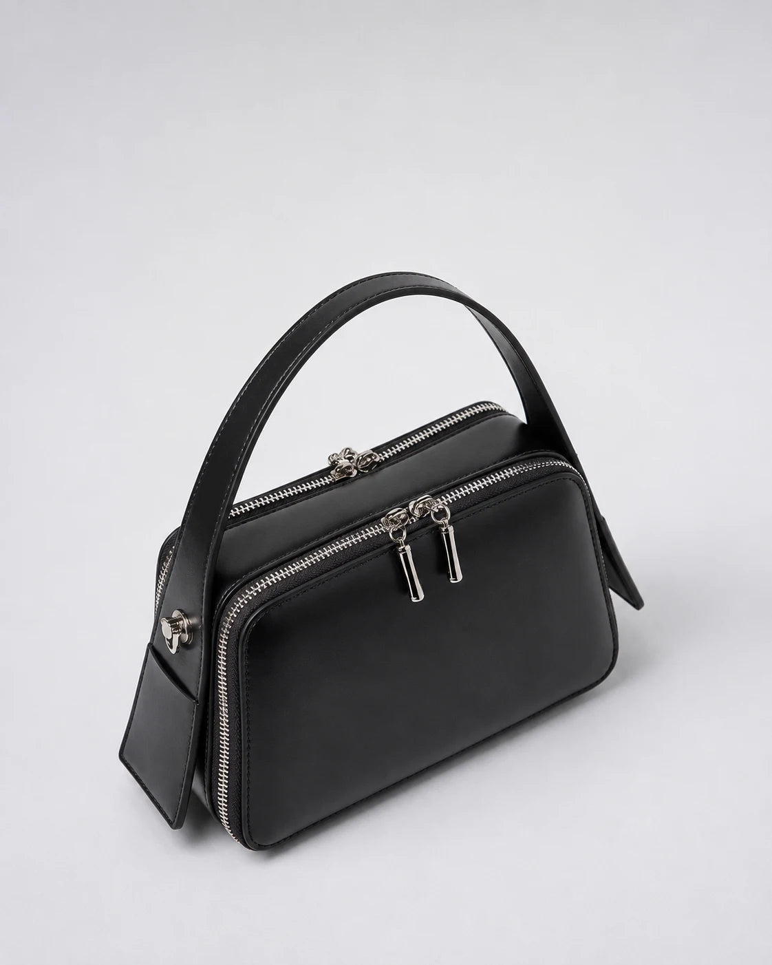 Bolsa feminina de couro preta Elyra em vista angular, mostrando alça de mão, compartimentos com fechamento em zíper e estrutura compacta.