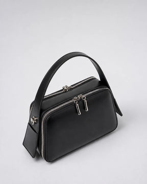 Bolsa feminina de couro preta Elyra em vista angular, mostrando alça de mão, compartimentos com fechamento em zíper e estrutura compacta.
