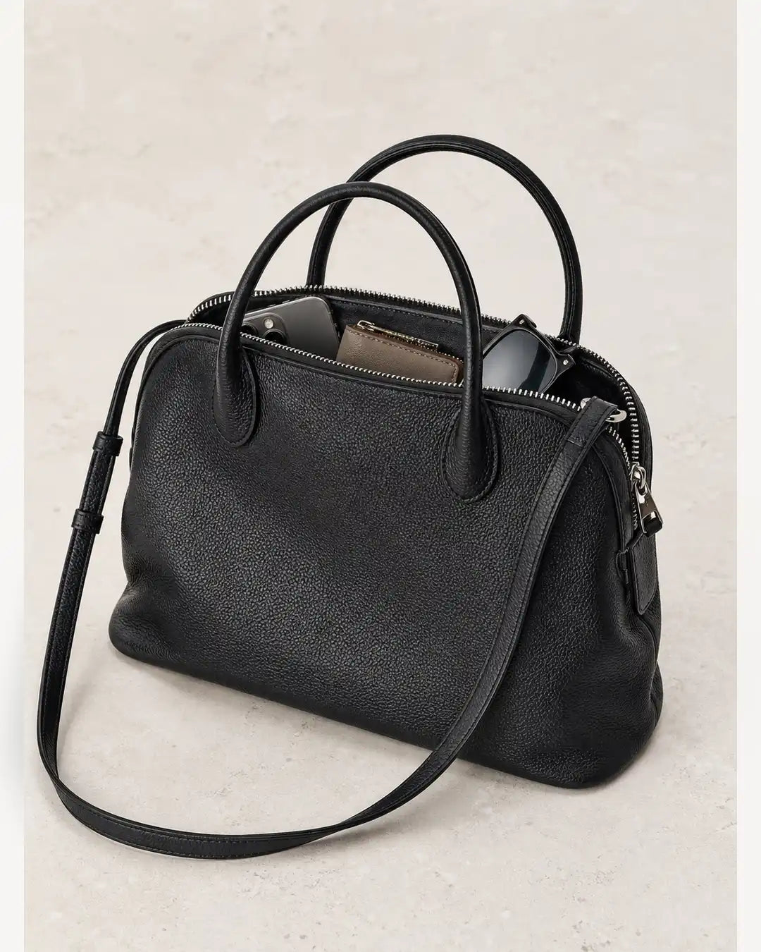 Bolsa feminina de couro preta Vivienne aberta, com celular, carteira e óculos no interior.