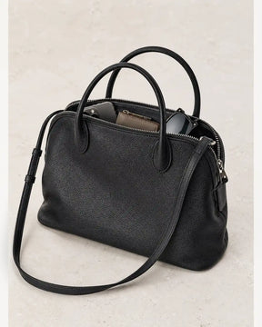 Bolsa feminina de couro preta Vivienne aberta, com celular, carteira e óculos no interior.