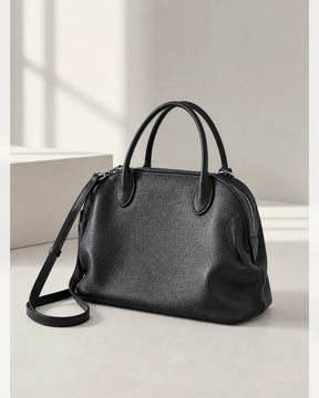 Bolsa feminina de couro preta Vivienne em estúdio claro, com alças de mão e alça transversal ajustável.