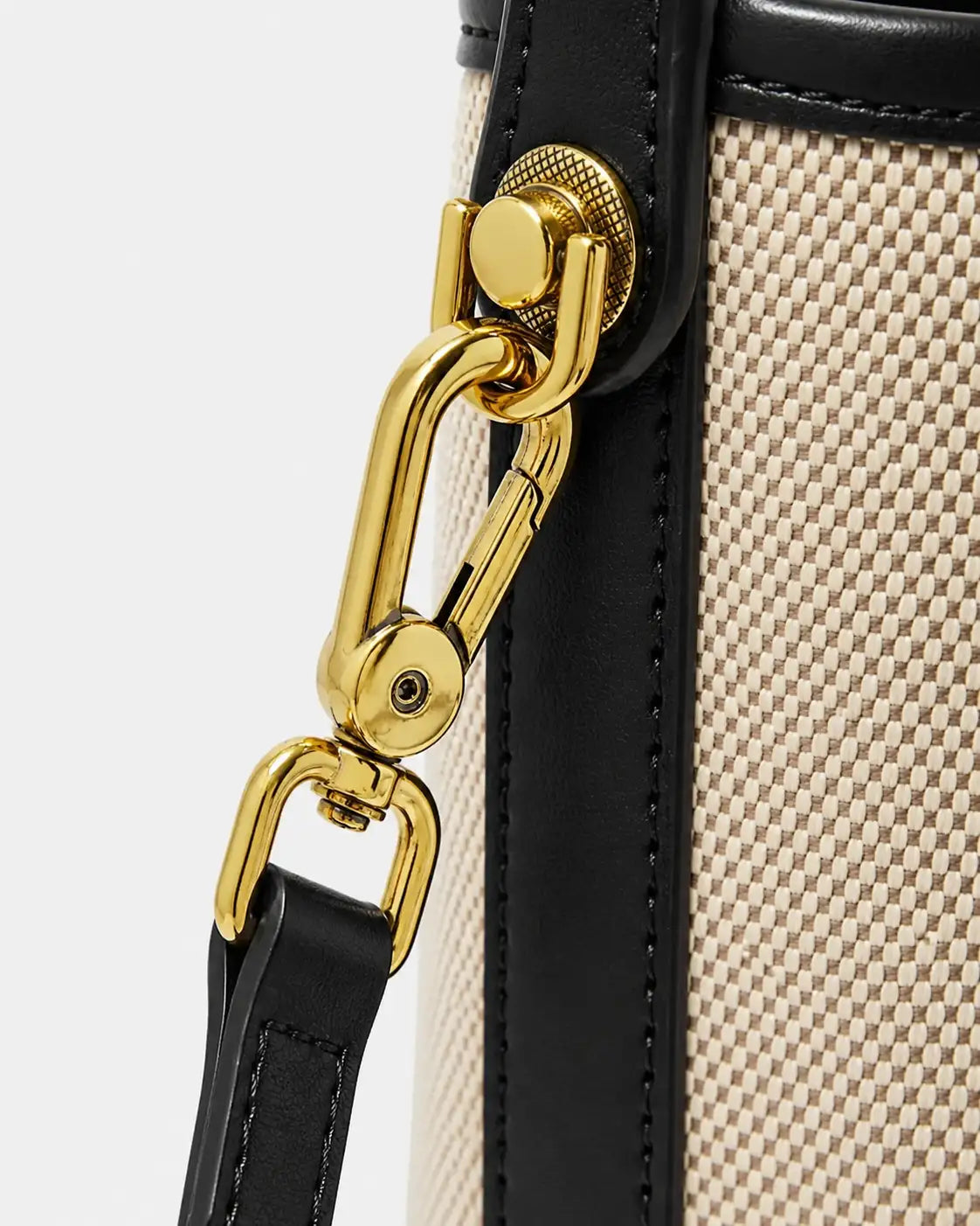 Detalhe da fixação lateral da alça transversal da bolsa feminina de ombro preta Lisette, com mosquetão dourado e acabamento preto.
