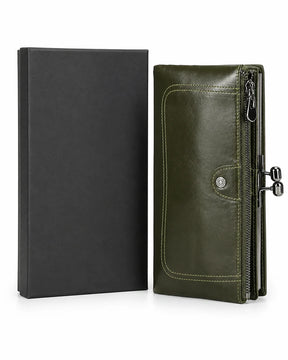 Carteira feminina de couro green Delphine posicionada ao lado de uma caixa preta, com design alongado, bolso externo com zíper e fecho metálico lateral.
