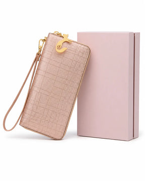 Carteira feminina de couro rose Aurielle posicionada ao lado de uma caixa rosa, com formato alongado, alça de mão e pingente dourado em formato de gato.
