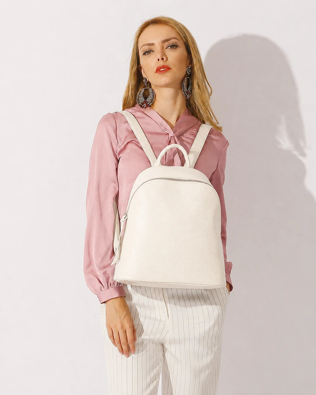 Mulher usando a mochila feminina de couro branca Aveline nas costas, destacando o tamanho, o caimento e o estilo elegante da peça.
