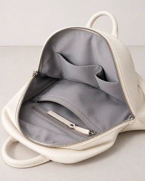 Mochila feminina de couro branca Aveline aberta, mostrando o interior com forro cinza, bolso interno com zíper e compartimentos organizadores.
