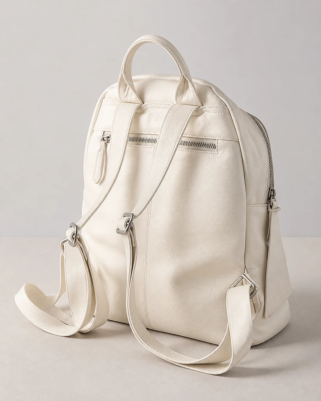 Mochila feminina de couro branca Aveline em vista traseira, com alça de mão, alças ajustáveis, bolso externo com zíper e acabamento macio.

