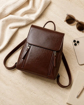 Mochila feminina de couro café Corinne em composição com acessórios, destacando o design elegante e a praticidade no dia a dia.