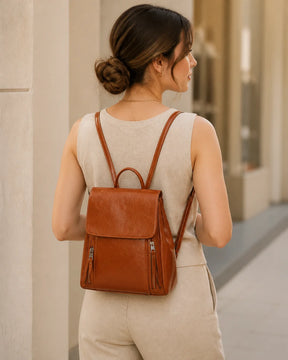 Mulher usando a mochila feminina de couro marrom Corinne nas costas, mostrando caimento, tamanho e estilo casual elegante.