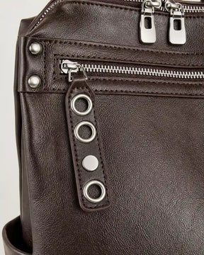Detalhe da mochila feminina de couro marrom Lorien, destacando o bolso frontal com zíper, os metais decorativos e o acabamento sofisticado.
