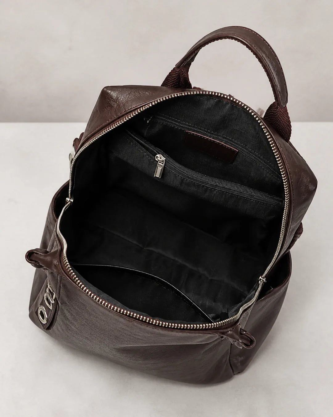 Mochila feminina de couro marrom Lorien aberta, exibindo o interior espaçoso com compartimentos internos e bolso com zíper para melhor organização.
