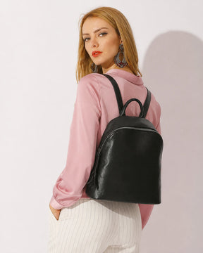Mulher usando a mochila feminina de couro preta Aveline nas costas, destacando o tamanho, o caimento e o visual elegante da peça.
