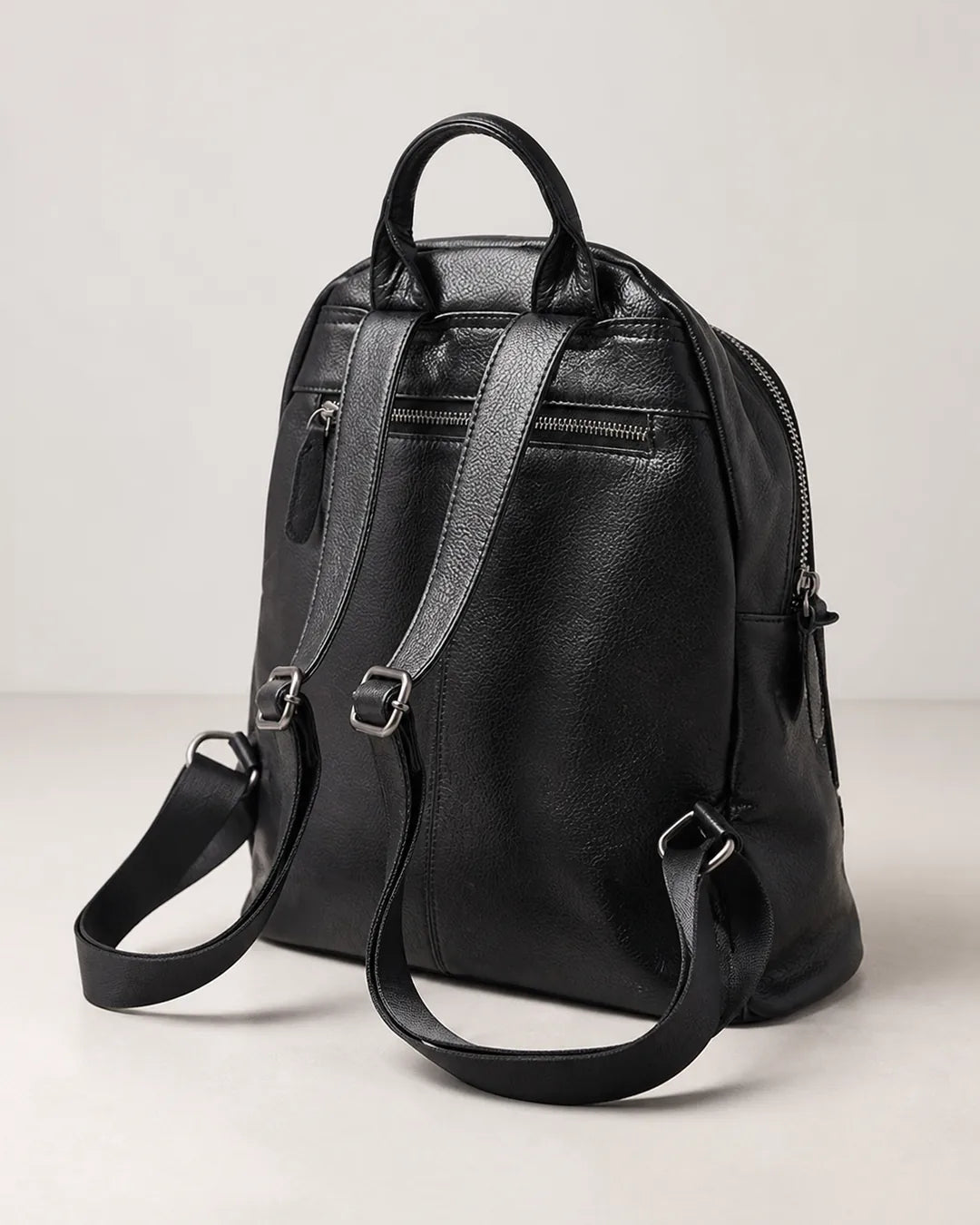 Mochila feminina de couro preta Aveline em vista traseira, com alça de mão, alças ajustáveis, bolso externo com zíper e acabamento macio.