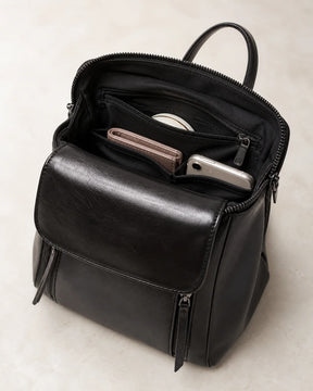 Mochila feminina de couro preta Corinne aberta, mostrando compartimentos internos para carteira, celular e objetos pessoais.