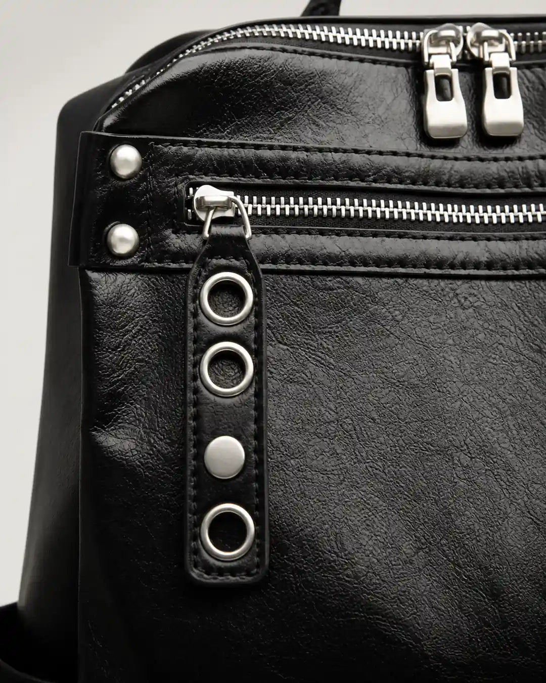 Detalhe da mochila feminina de couro preta Lorien, mostrando o bolso frontal com zíper, puxador decorativo com ilhós metálicos e acabamento sofisticado.