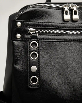 Detalhe da mochila feminina de couro preta Lorien, mostrando o bolso frontal com zíper, puxador decorativo com ilhós metálicos e acabamento sofisticado.