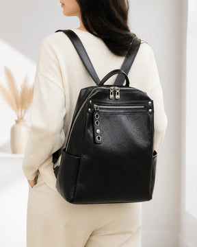 Mulher usando a mochila feminina de couro preta Lorien nas costas, mostrando o caimento, o tamanho e o visual elegante da peça.
