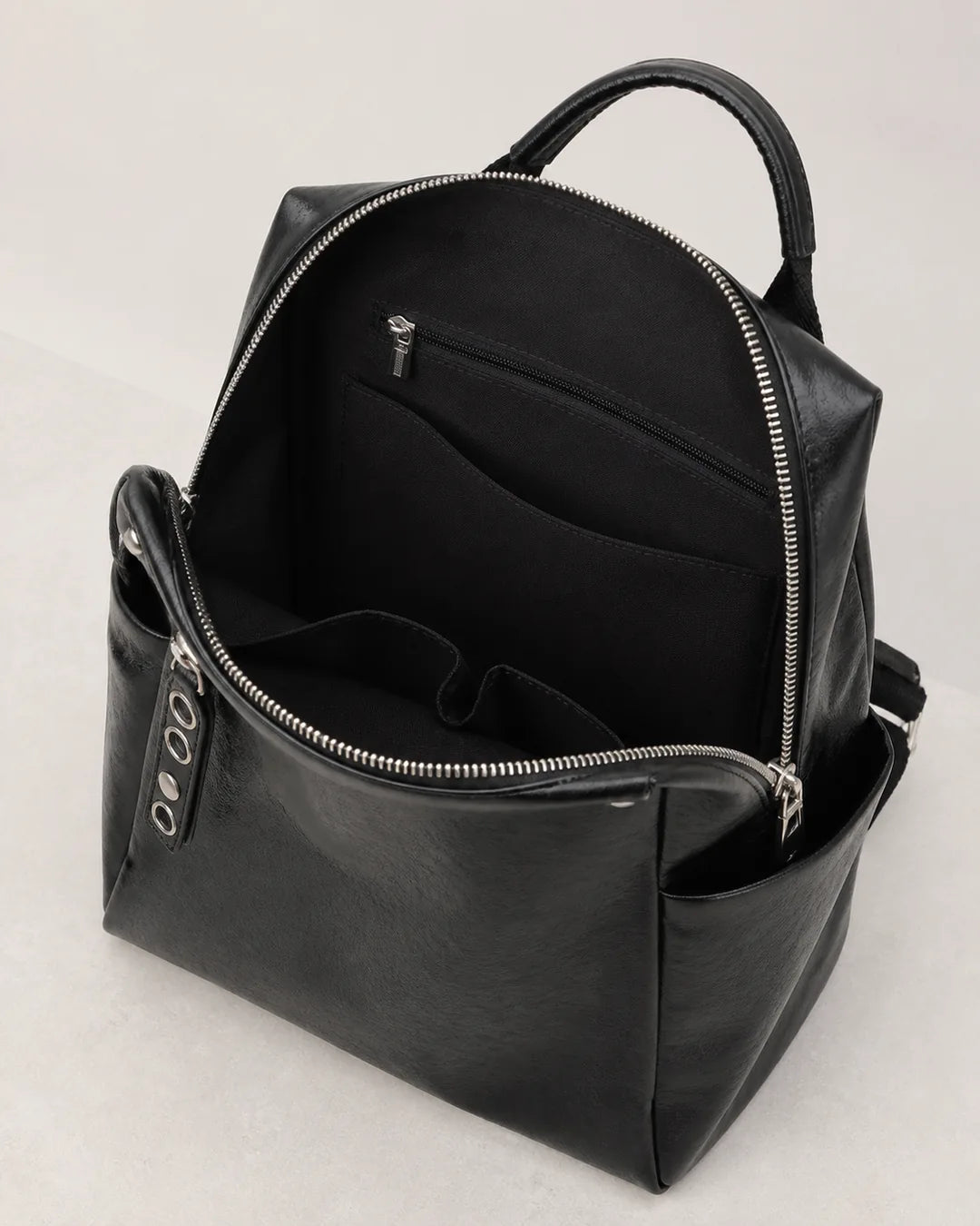 Mochila feminina de couro preta Lorien aberta, exibindo o interior espaçoso com divisórias internas e bolso com zíper para melhor organização.
