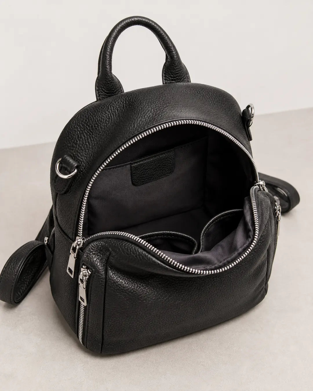 Mochila feminina de couro preta Serelle aberta, exibindo o interior espaçoso com forro escuro e divisórias internas para melhor organização.

