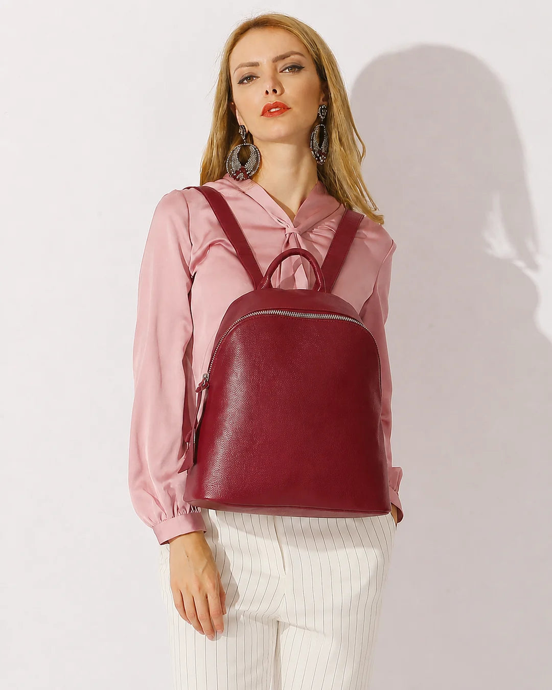 Mulher usando a mochila feminina de couro vermelha Aveline nas costas, destacando o tamanho, o caimento e o visual elegante da peça.

