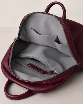 Mochila feminina de couro vermelha Aveline aberta, mostrando o interior com forro cinza, bolso interno com zíper e compartimentos organizadores.
